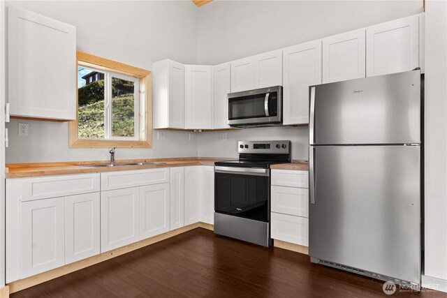 kitchen with a sink, butcher block counters, stainless steel appliances, white cabinetry, and dark wood-type flooring