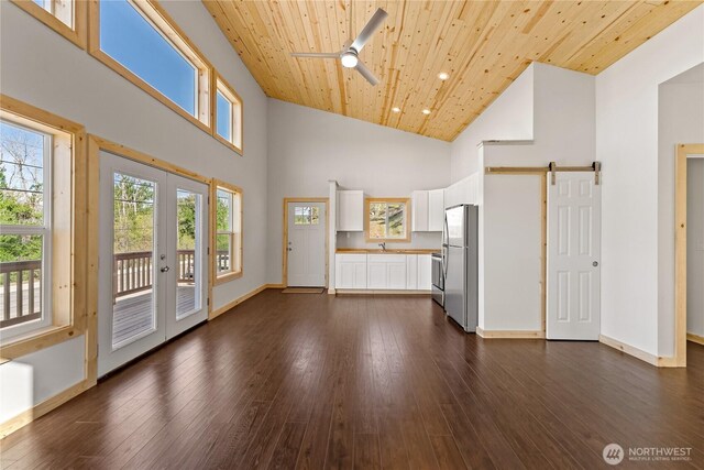 unfurnished living room with ceiling fan, a barn door, high vaulted ceiling, french doors, and wood ceiling