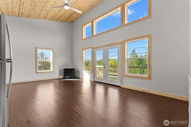 unfurnished living room featuring a wood stove, baseboards, a high ceiling, hardwood / wood-style flooring, and a ceiling fan