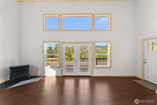 interior space with a wood stove, french doors, baseboards, a towering ceiling, and hardwood / wood-style flooring