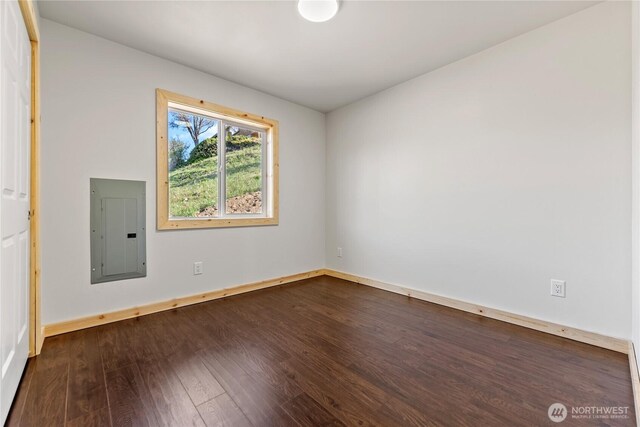 unfurnished room featuring baseboards, dark wood finished floors, and electric panel