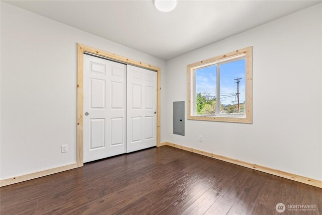 unfurnished bedroom featuring a closet, baseboards, dark wood finished floors, and electric panel