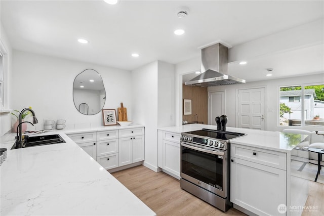 kitchen with a sink, a peninsula, light wood-type flooring, island exhaust hood, and electric stove