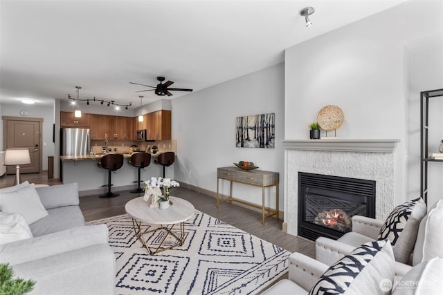 living room featuring baseboards, a glass covered fireplace, ceiling fan, and wood finished floors