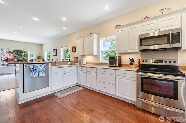 kitchen with white cabinets, stainless steel appliances, recessed lighting, a peninsula, and wood finished floors