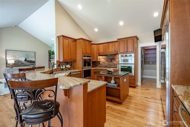 kitchen featuring a sink, stainless steel appliances, light wood-style flooring, backsplash, and lofted ceiling