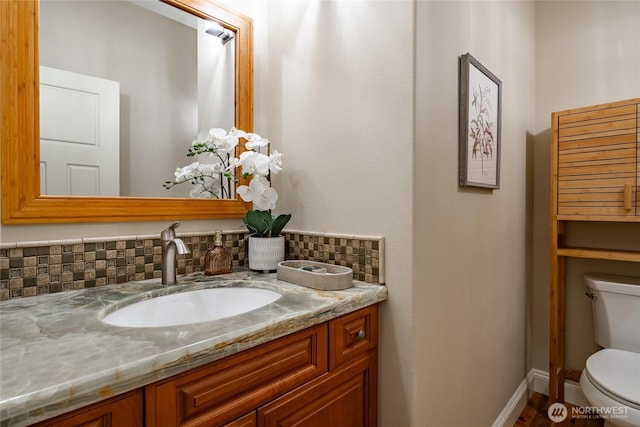 bathroom featuring toilet, vanity, baseboards, and decorative backsplash