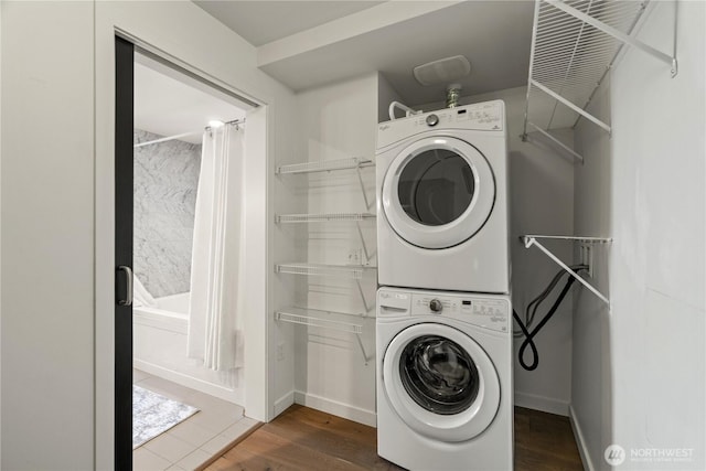 laundry area with laundry area, stacked washer and dryer, baseboards, and wood finished floors