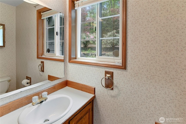 bathroom featuring vanity, toilet, and wallpapered walls