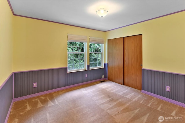 unfurnished bedroom featuring crown molding, carpet, wainscoting, and a closet