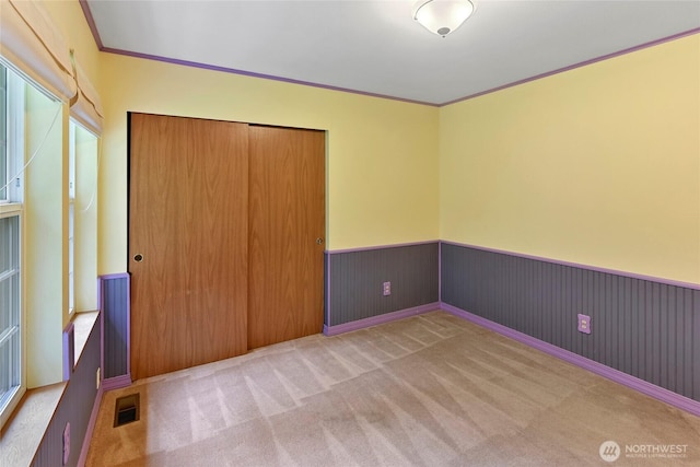 unfurnished bedroom featuring visible vents, crown molding, wainscoting, a closet, and carpet