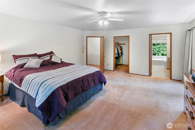 bedroom with a closet, light carpet, ensuite bathroom, a walk in closet, and a ceiling fan