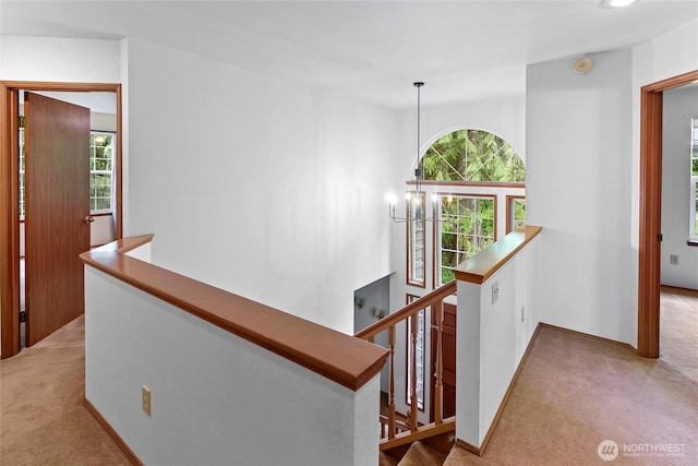 hall with light colored carpet, baseboards, and an upstairs landing