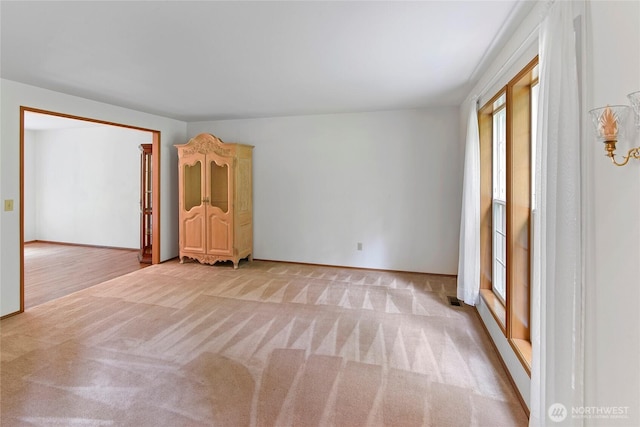 empty room featuring plenty of natural light, baseboards, visible vents, and light colored carpet