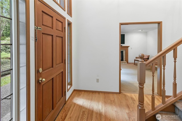 foyer entrance featuring a fireplace with raised hearth, baseboards, light wood finished floors, and stairway