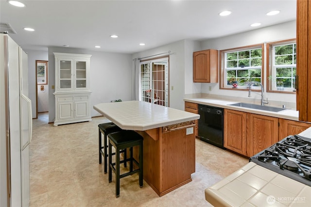 kitchen featuring a sink, black dishwasher, tile countertops, freestanding refrigerator, and a kitchen island