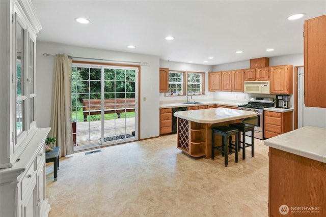 kitchen with a sink, gas stove, recessed lighting, white microwave, and visible vents