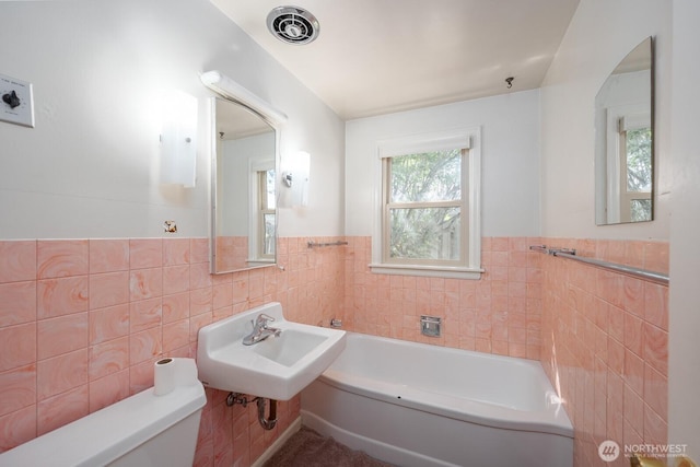 bathroom with a bath, tile walls, a sink, a wainscoted wall, and toilet