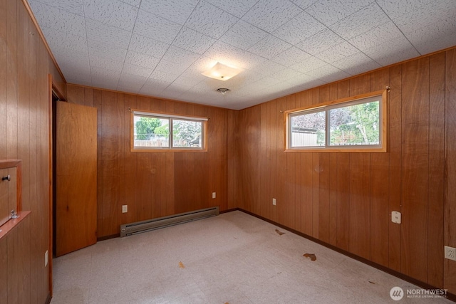 unfurnished room with wooden walls, tile patterned floors, visible vents, and a baseboard radiator