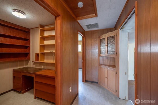 unfurnished office with wooden walls, baseboards, visible vents, and built in study area