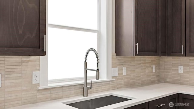 kitchen with light countertops, dark brown cabinets, a sink, and tasteful backsplash