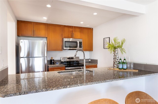 kitchen with brown cabinetry, a peninsula, recessed lighting, dark stone counters, and stainless steel appliances