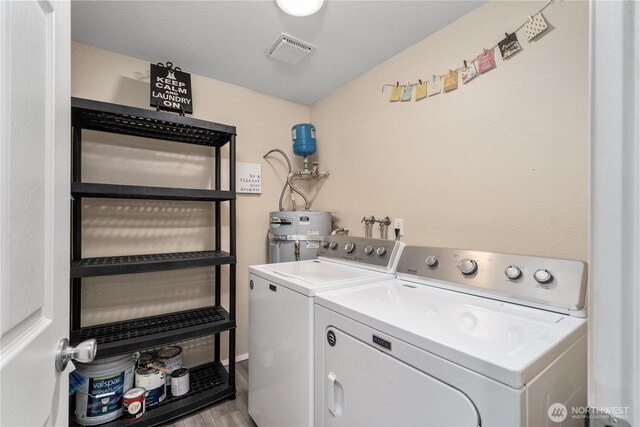 washroom featuring visible vents, laundry area, wood finished floors, electric water heater, and independent washer and dryer
