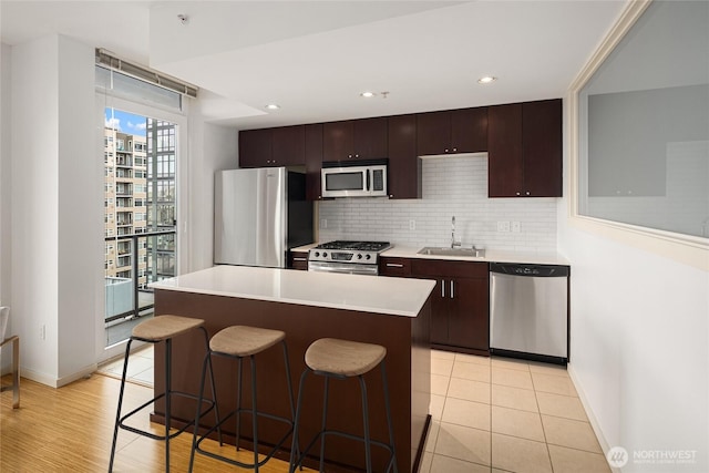 kitchen featuring decorative backsplash, a kitchen breakfast bar, a sink, baseboards, and stainless steel appliances
