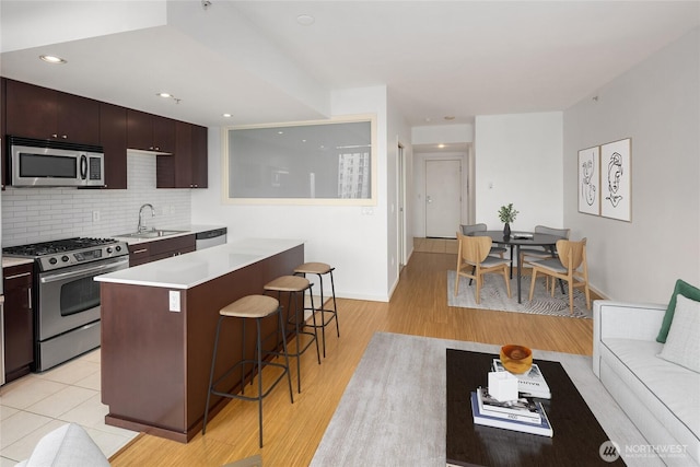 kitchen with decorative backsplash, a kitchen breakfast bar, light countertops, a sink, and stainless steel appliances