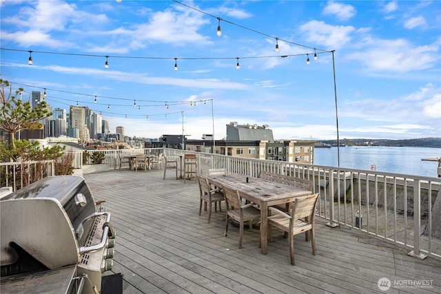 deck with a water view, outdoor dining space, and a grill