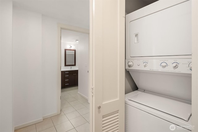 laundry area with laundry area, stacked washing maching and dryer, baseboards, a sink, and light tile patterned flooring