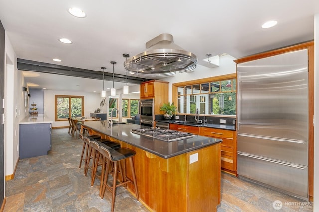 kitchen with dark countertops, recessed lighting, brown cabinets, a sink, and stone finish flooring