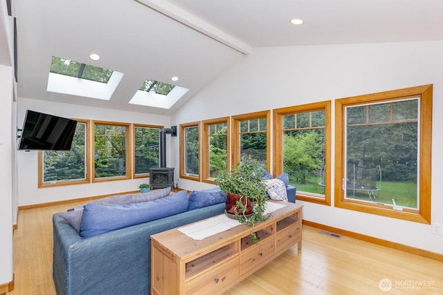 living area featuring visible vents, a wood stove, baseboards, light wood-type flooring, and vaulted ceiling with skylight