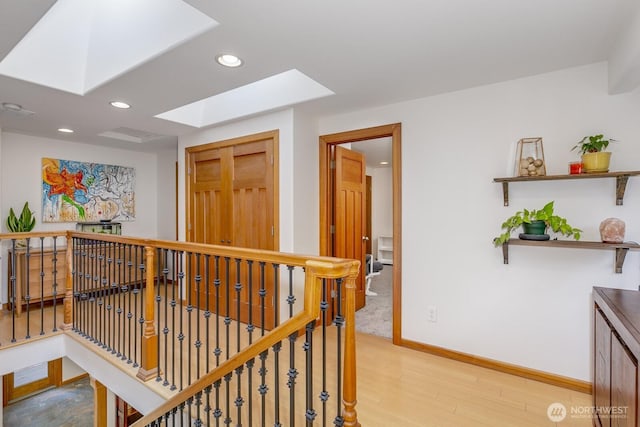corridor featuring a skylight, baseboards, an upstairs landing, light wood-style floors, and recessed lighting