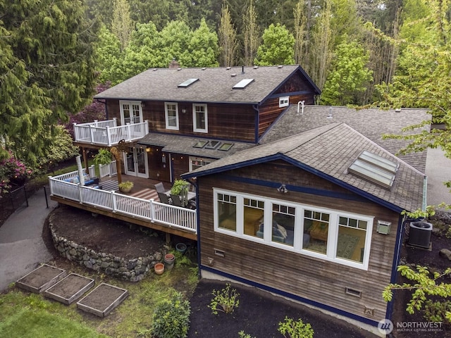 back of property with a shingled roof, central AC, a wooden deck, a forest view, and french doors
