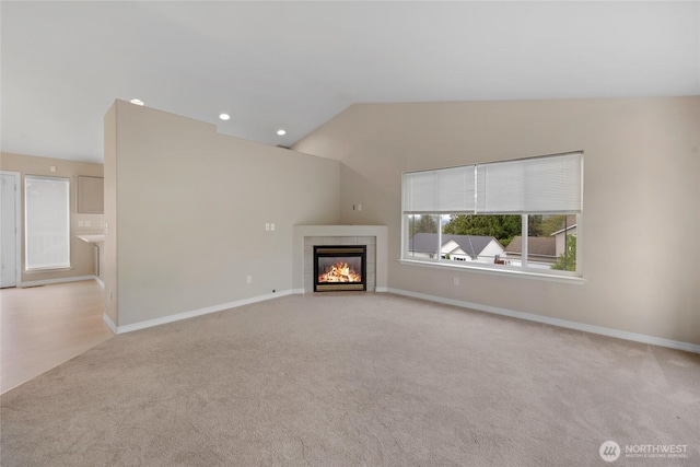 unfurnished living room featuring a tiled fireplace, baseboards, lofted ceiling, carpet flooring, and recessed lighting