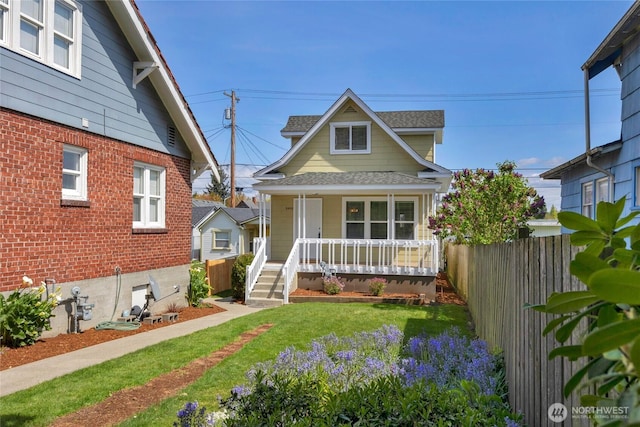 view of front of property with fence, a shingled roof, a porch, and a front lawn