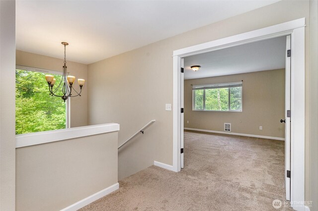 hallway with an inviting chandelier, visible vents, baseboards, carpet, and an upstairs landing