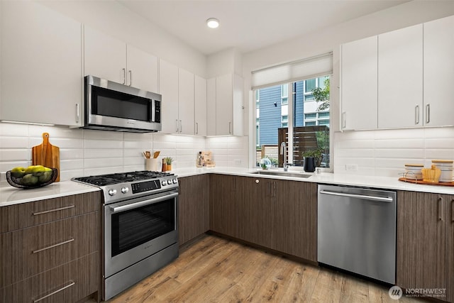 2414 NW 64th St Unit A, Seattle, WA 98107 - kitchen with appliances with stainless steel finishes, a sink, light countertops, white cabinets, and light wood-style flooring