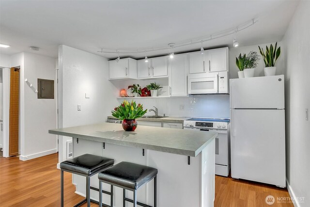 kitchen with a kitchen breakfast bar, white cabinetry, a sink, white appliances, and light wood-style flooring