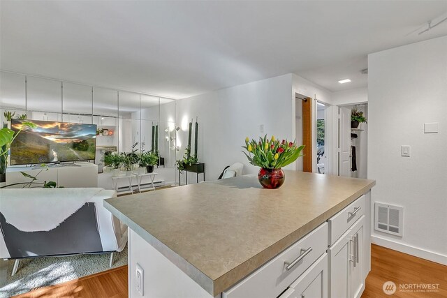 kitchen featuring visible vents, a center island, baseboards, white cabinets, and light wood-style flooring