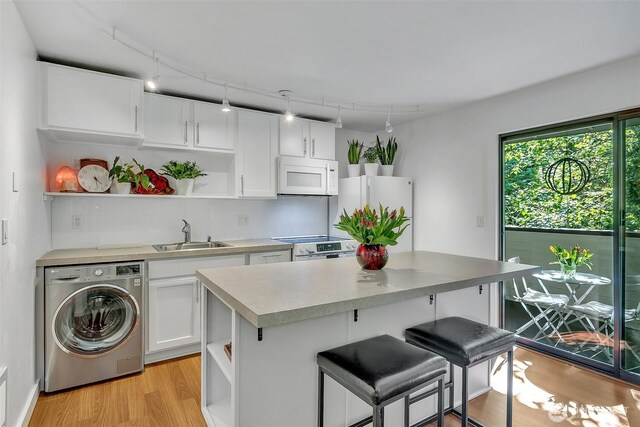 kitchen with open shelves, washer / dryer, white appliances, light wood-type flooring, and a sink