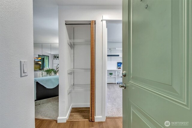 hallway with baseboards, a textured wall, and wood finished floors