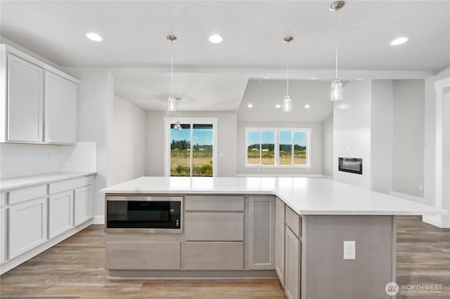kitchen featuring a large fireplace, built in microwave, light wood-type flooring, light countertops, and recessed lighting