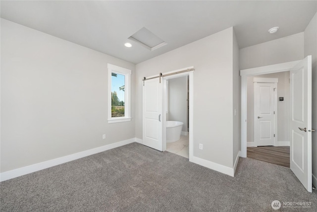 unfurnished bedroom with baseboards, ensuite bathroom, attic access, a barn door, and carpet flooring