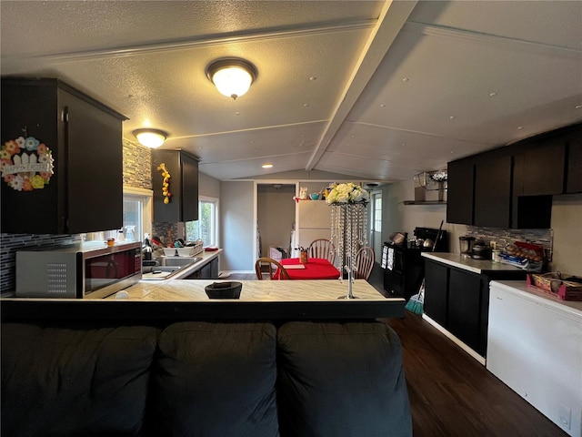 kitchen featuring dark wood-style flooring, a healthy amount of sunlight, vaulted ceiling with beams, stainless steel microwave, and a sink
