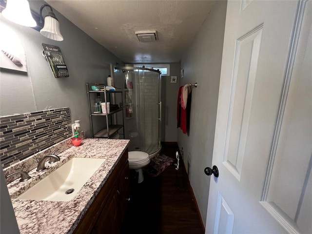 bathroom with backsplash, a shower stall, wood finished floors, vanity, and toilet