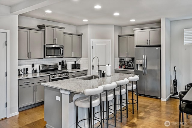 kitchen with a sink, gray cabinets, a kitchen island with sink, and stainless steel appliances