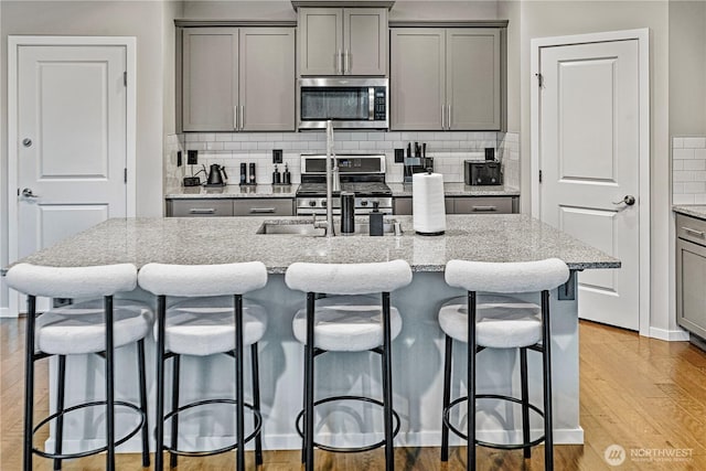 kitchen with light wood-style flooring, appliances with stainless steel finishes, backsplash, and gray cabinetry