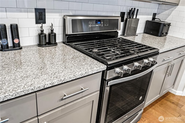 kitchen with stainless steel gas range, light stone countertops, decorative backsplash, and light wood-style flooring